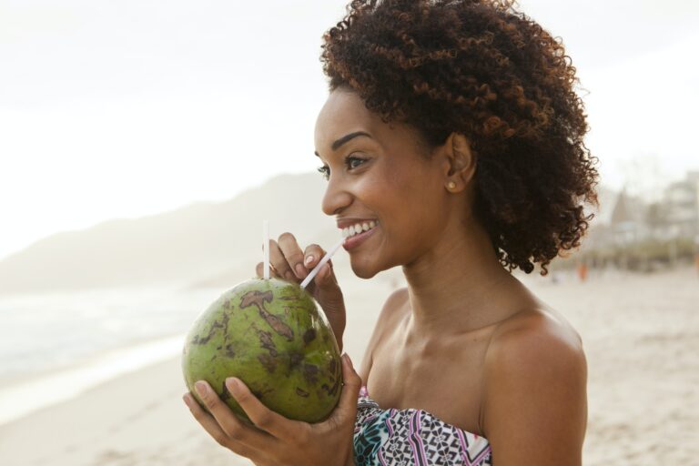 Portrait of young woman drinking coconut milk on beach, Rio De Janeiro, Brazil